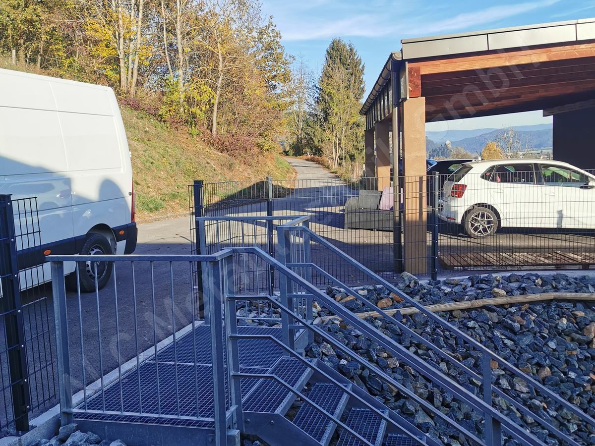Anthrazitfarbener Doppelstabmattenzaun entlang einer Einfahrt neben Carport und verzinkter Au&szlig;enstiege