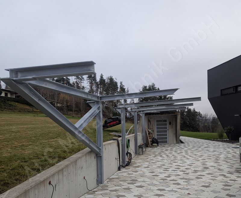 Feuerverzinkte Stahlkonstruktion eines Carports im Rohbau auf Betonmauer vor modernem Neubau