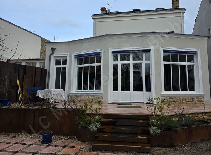 Terrasse mit Beeteinfassung und Stufen aus Cortenstahl vor einem sanierten Wohnhaus