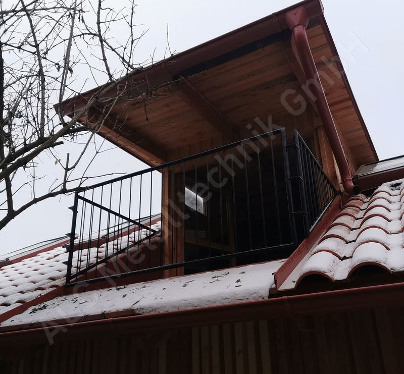 Balkongel&auml;nder aus anthrazitem Stahl mit senkrechten Rundst&auml;ben an einem Holzhaus im Winter