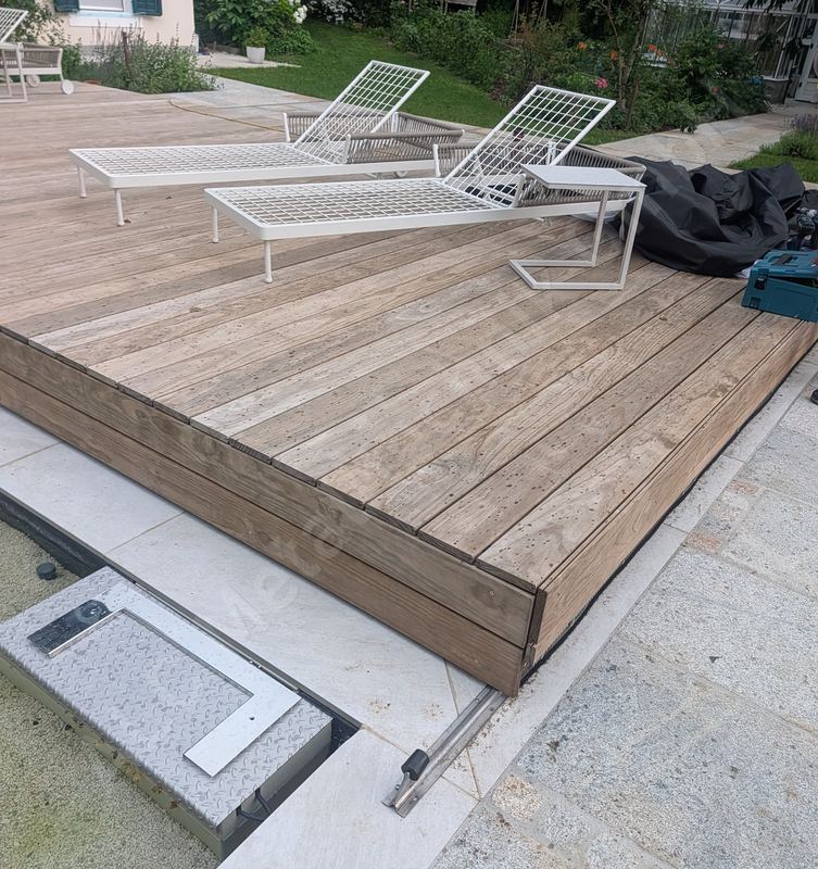 Pooldeck aus Holz mit Liegen, daneben der offene Technikschacht mit dem Antrieb der Abdeckung