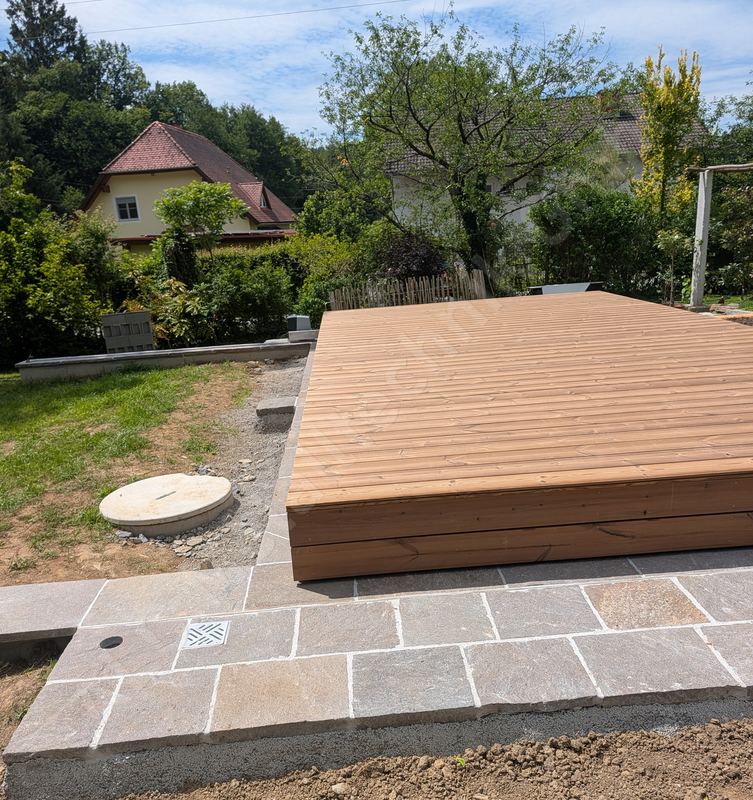 Geschlossenes Pooldeck aus L&auml;rchenholz mit Natursteineinfassung im sonnigen Garten