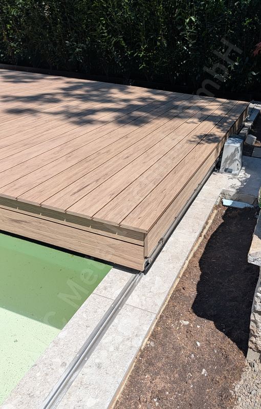 Halb ge&ouml;ffnete Poolabdeckung in Holzoptik, darunter das Poolwasser, Laufschiene im Natursteinrand