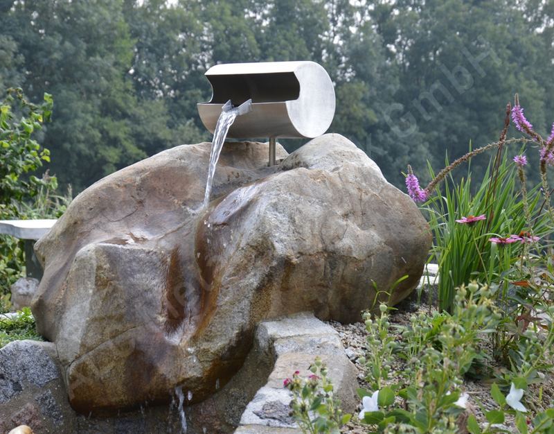Wasserspeier aus Edelstahl &uuml;ber einem Findling am Gartenteich