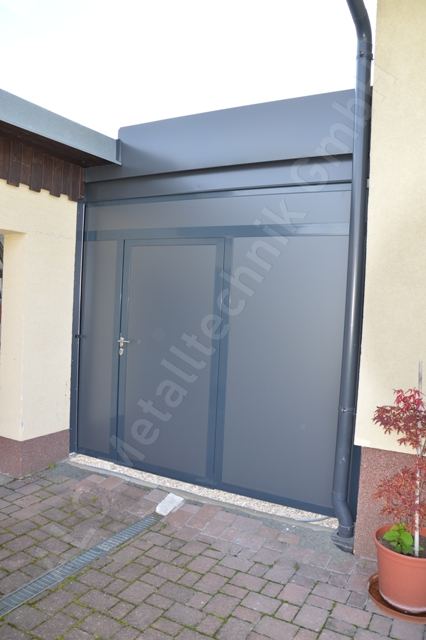 Sichtschutzwand aus anthrazit beschichtetem Metall mit Tür, schließt den Durchgang zwischen Haus und Nebengebäude